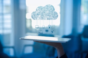 Illustration of cloud with hanging icons being projected our of an electronic tablet.