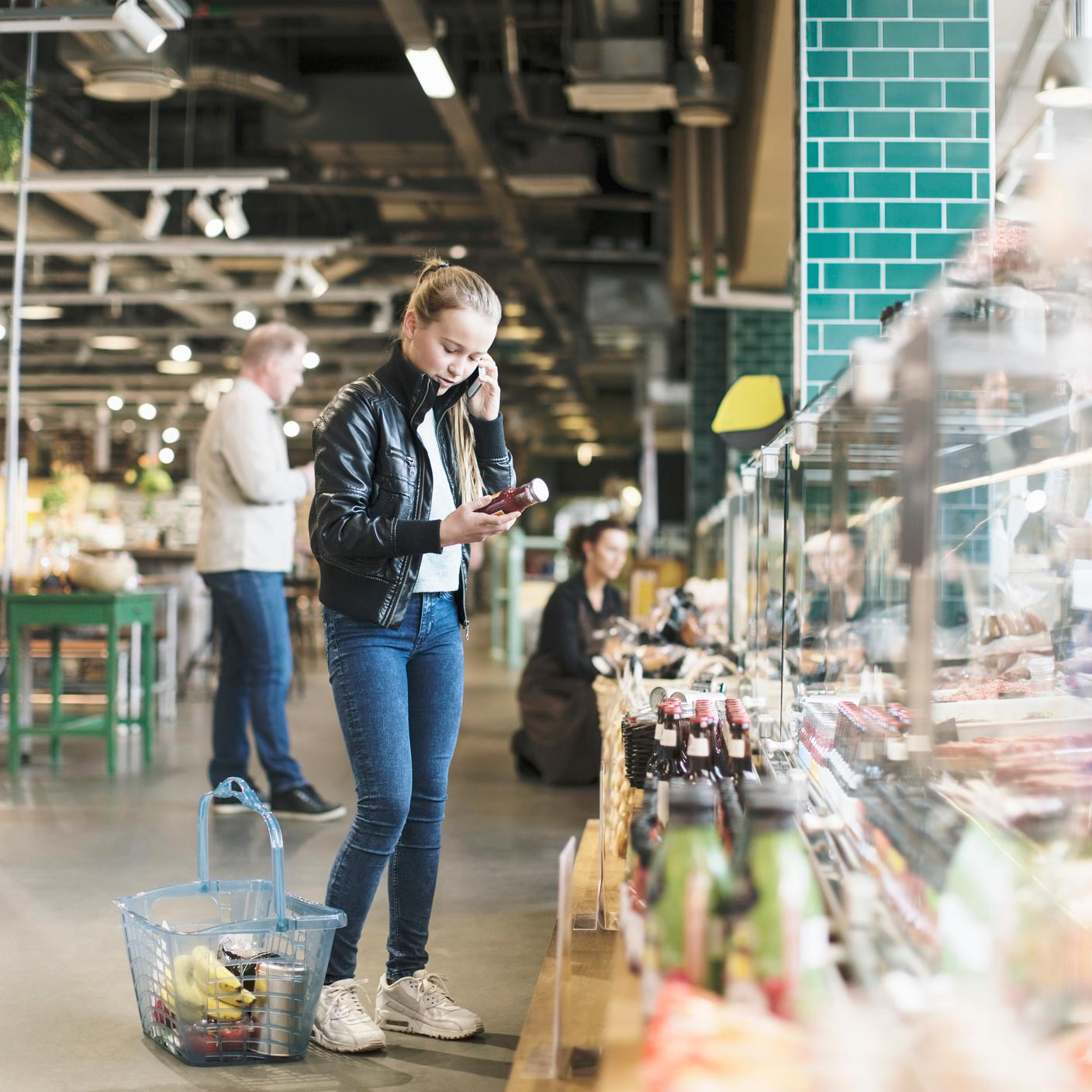 deterring food attacks - Girl using smart phone reading label in organic groceries store