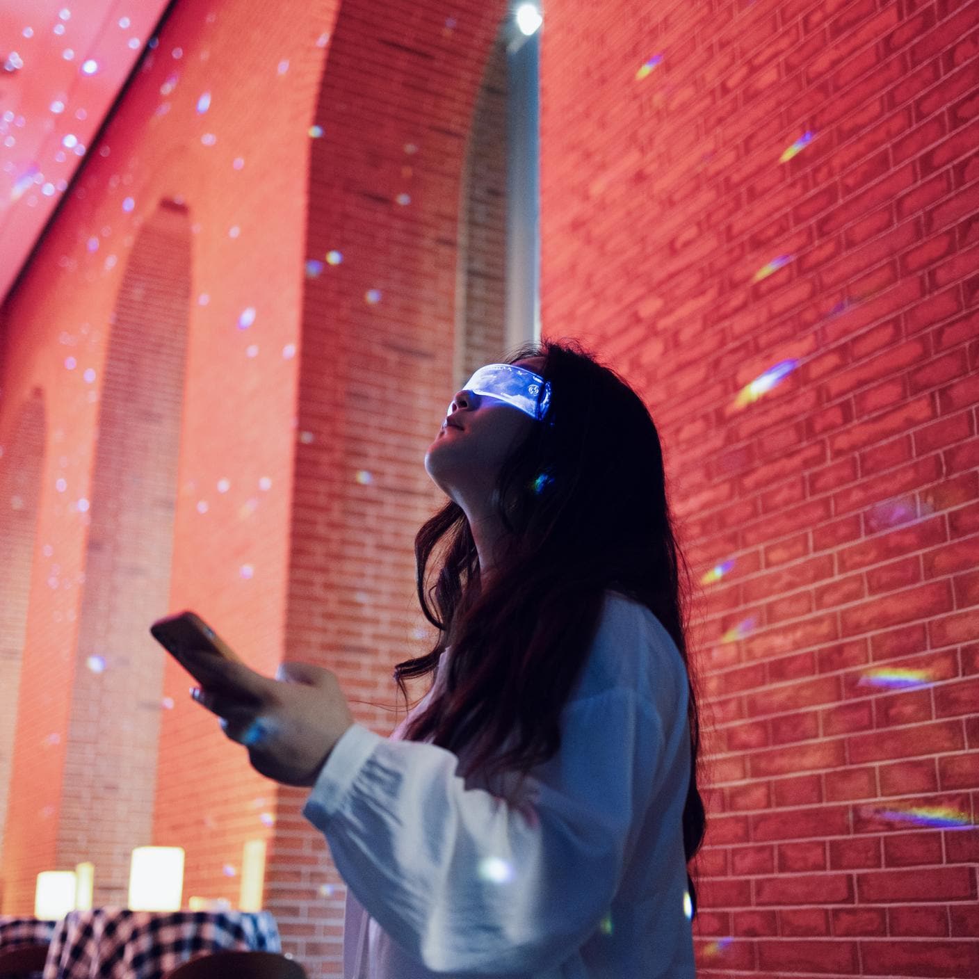 Woman wearing augmented reality glasses standing in night street using smartphone