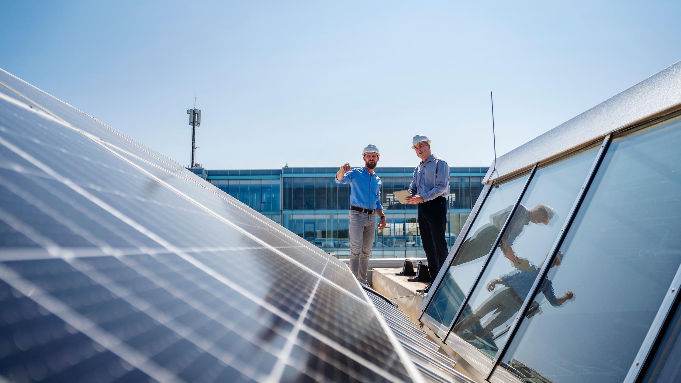 Two businessmen in hard hats meeting on the roof of a company building with solar panels