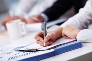 Person sat, writing on clipboard in business meeting.