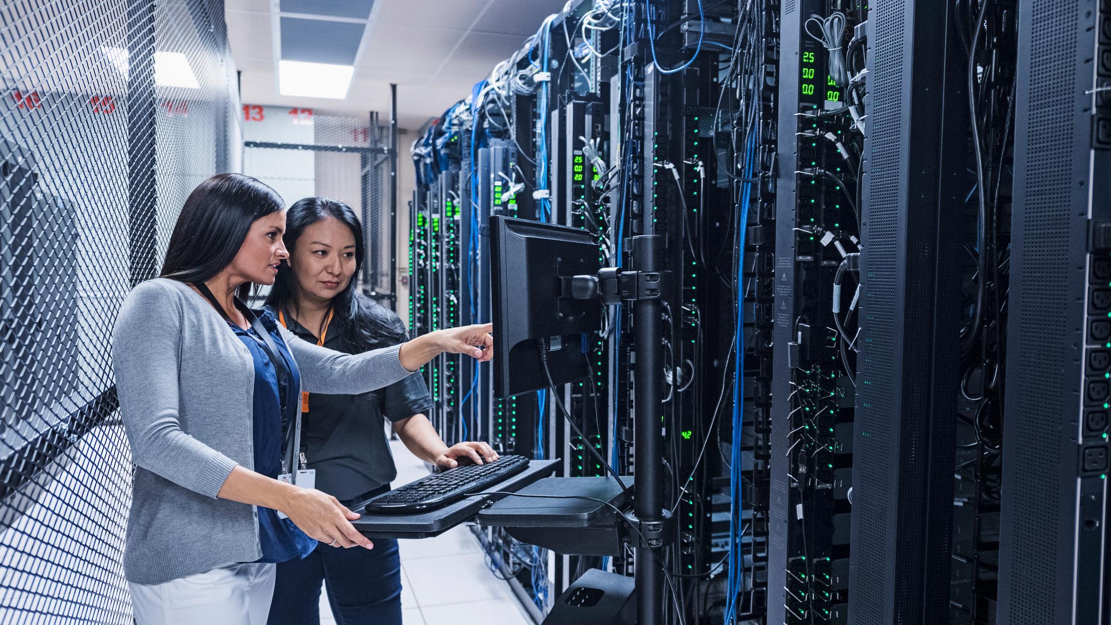 Twee vrouwelijke medewerkers in een groot datacenter voeren controles op servers uit