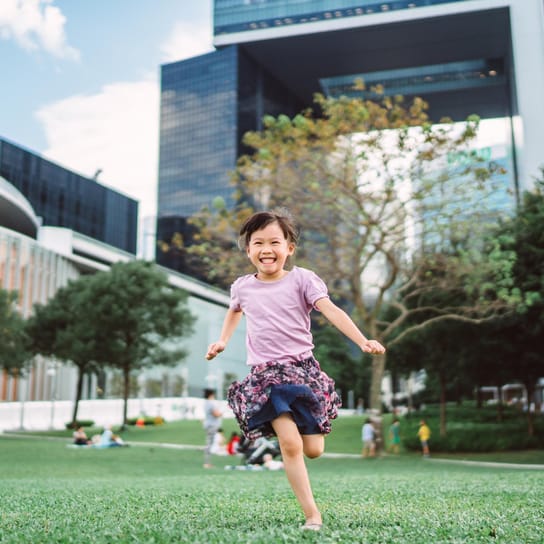 jeune fille qui court tout sourire entre des bâtiments verts