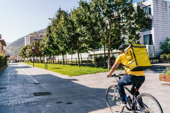 Food delivery man riding a bicycle with a yellow isothermal backpack in a small town, delivering foo