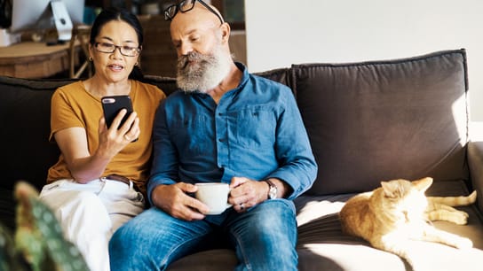 La marque Kitemark™ pour un service inclusif - Un couple de personnes âgées utilisant un téléphone pour faire des recherches sur Internet ensemble sur le canapé à la maison.