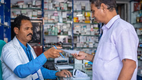 Customer asking medicine to pharmacist by showing doctor proscription at pharma retail store.