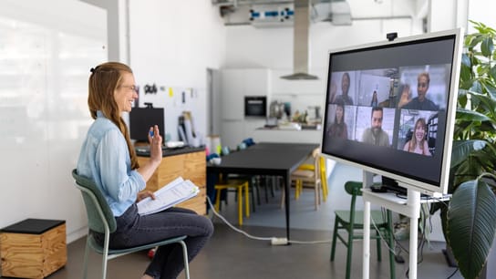 Professional having online meeting with team seen on big television screen.