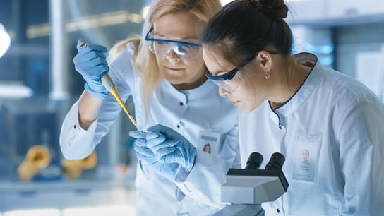 Innovationslabore – Eine medizinische Forschungswissenschaftlerin tropft eine Probe auf einen Objektträger und ihr Kollege untersucht sie unter dem Mikroskop