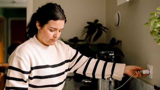 Woman charging smart phone while standing near kitchen counter at home