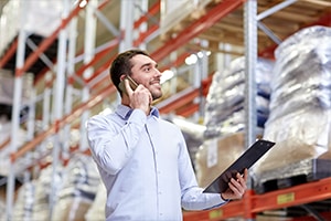 Man in warehouse on mobile phone, holding electronic tablet. 