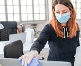 Frau mit Maske putzt Staub vom PC - ISO 45001 - Arbeits- und Gesundheitsschutz Fallstudie