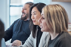 Three people working together in front of a computer monitor