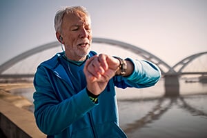 An elderly man checks his smartwatch while exercising outside
