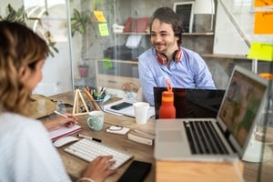 Two office workers conversing, divided by a plexiglass window