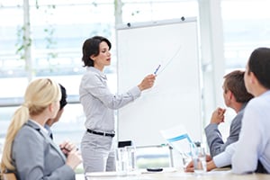 Business meeting with woman pointing at chart on freestanding white board.