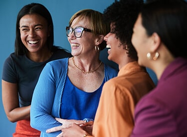 Group of diverse businesswomen laughing while standing together in front of a blue background