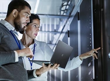 Two people surveying computer servers in a server room