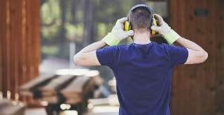 Man holding ear defenders with protective gloves.