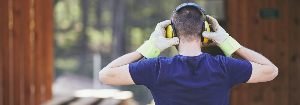 Man holding ear defenders with protective gloves.