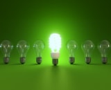 Illuminated energy efficient light bulb surrounded by none lit lightbulbs on green background.