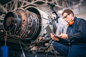 A mechanic working on a jet engine, and is looking at a tablet.