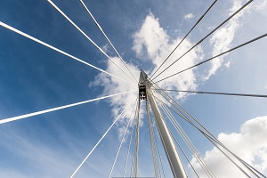 Looking up at bridge supports with blue sky and clouds above.