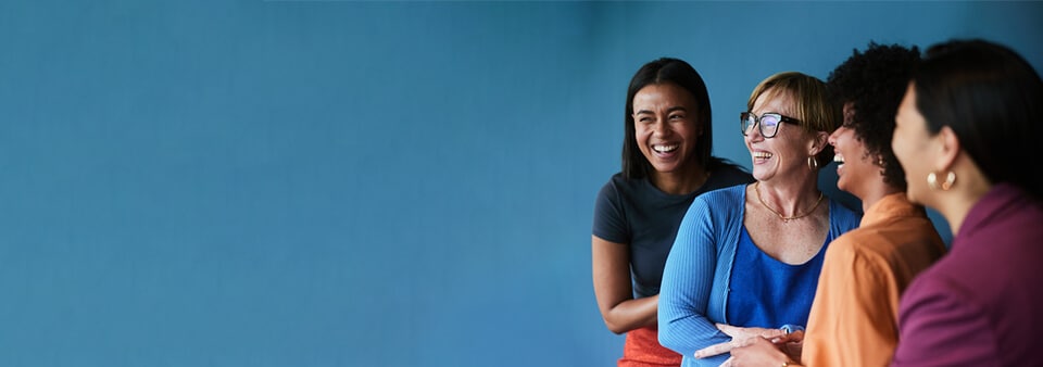 Group of diverse businesswomen laughing while standing together in front of a blue background