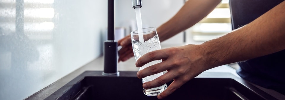young man pouring fresh water from kitchen sink