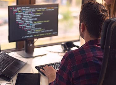 Man sitting in front of a computer monitor displaying code