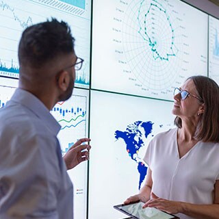 The Supply Chain Risk Insights Report reflects on 2022, the impact of a global pandemic, irreversible climate change, and geopolitical uncertainty. Two people look at a chart displaying data on a wall
