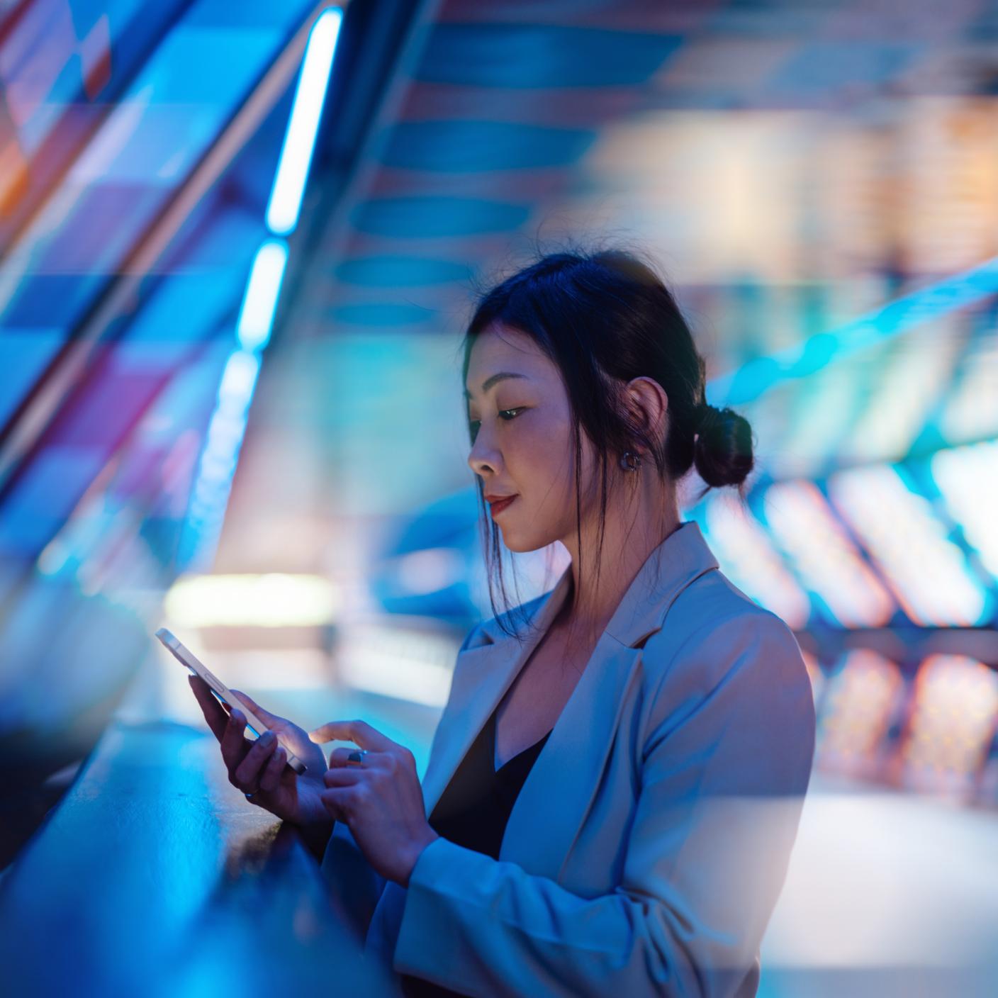 Young business woman holding smartphone with a computer generated background. Innovation, metaverse and futuristic concepts.