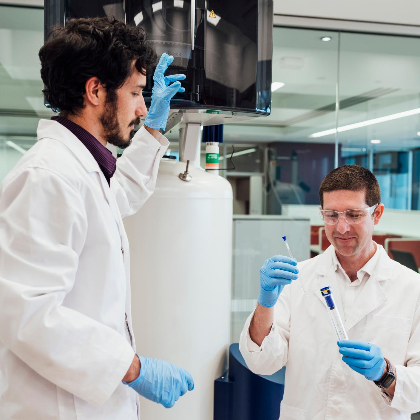 Two male scientists holding samples wearing protective clothing.