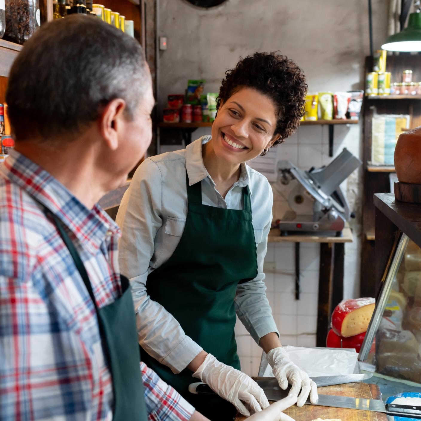 Cheerful saleswoman looking at her colleague working together in a charcuterie - People at work concepts