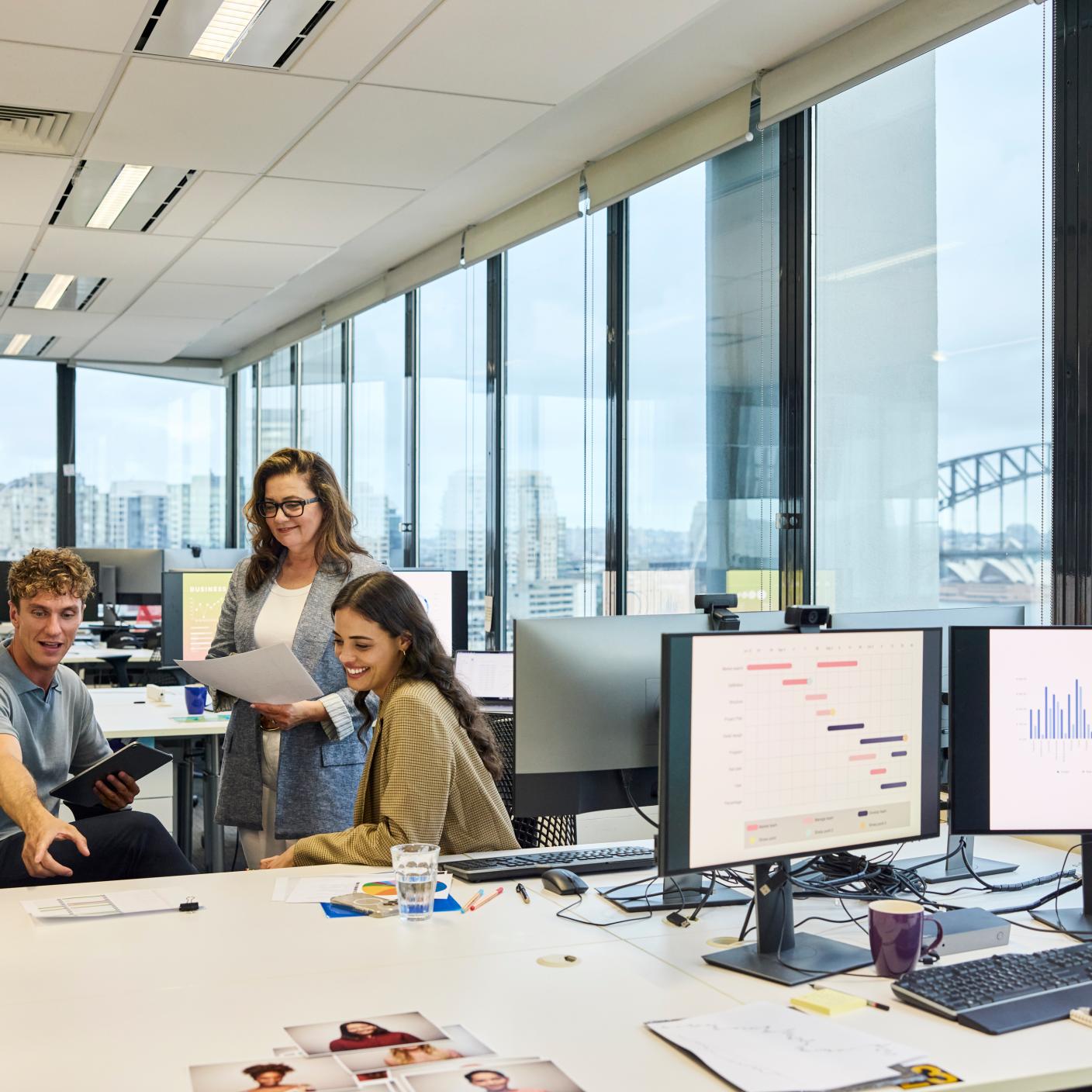 Multi racial colleagues planning strategies in team meeting at office. Male entrepreneur is pointing at reports. Computers are kept on desk.