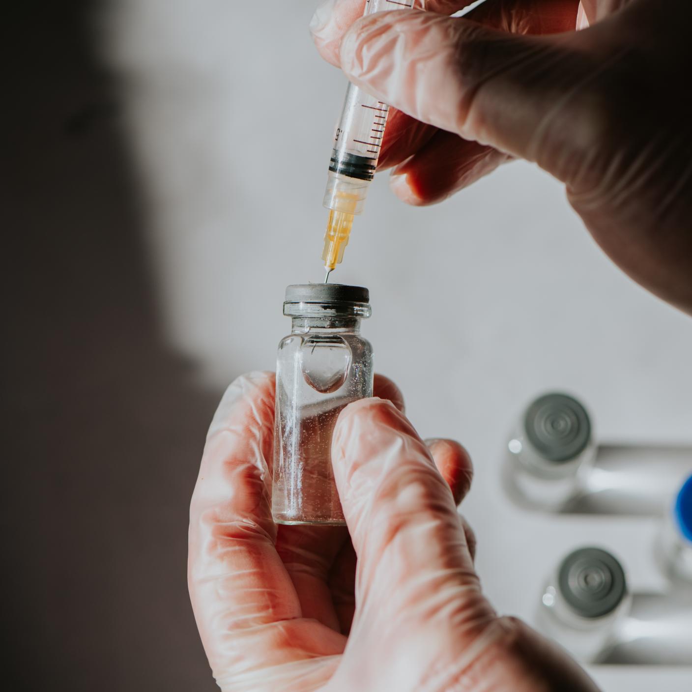 A healthcare professional uses a syringe to draw liquid medicine from a vial.