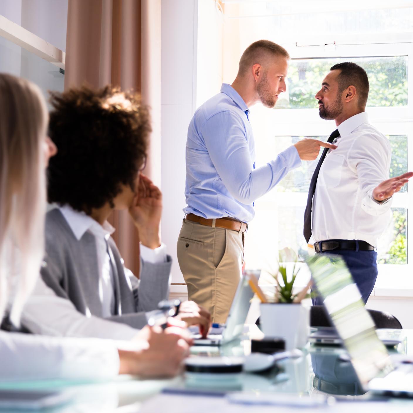 Stressed Businesspeople Sitting In Front Of Two Male Colleagues Fighting In Office