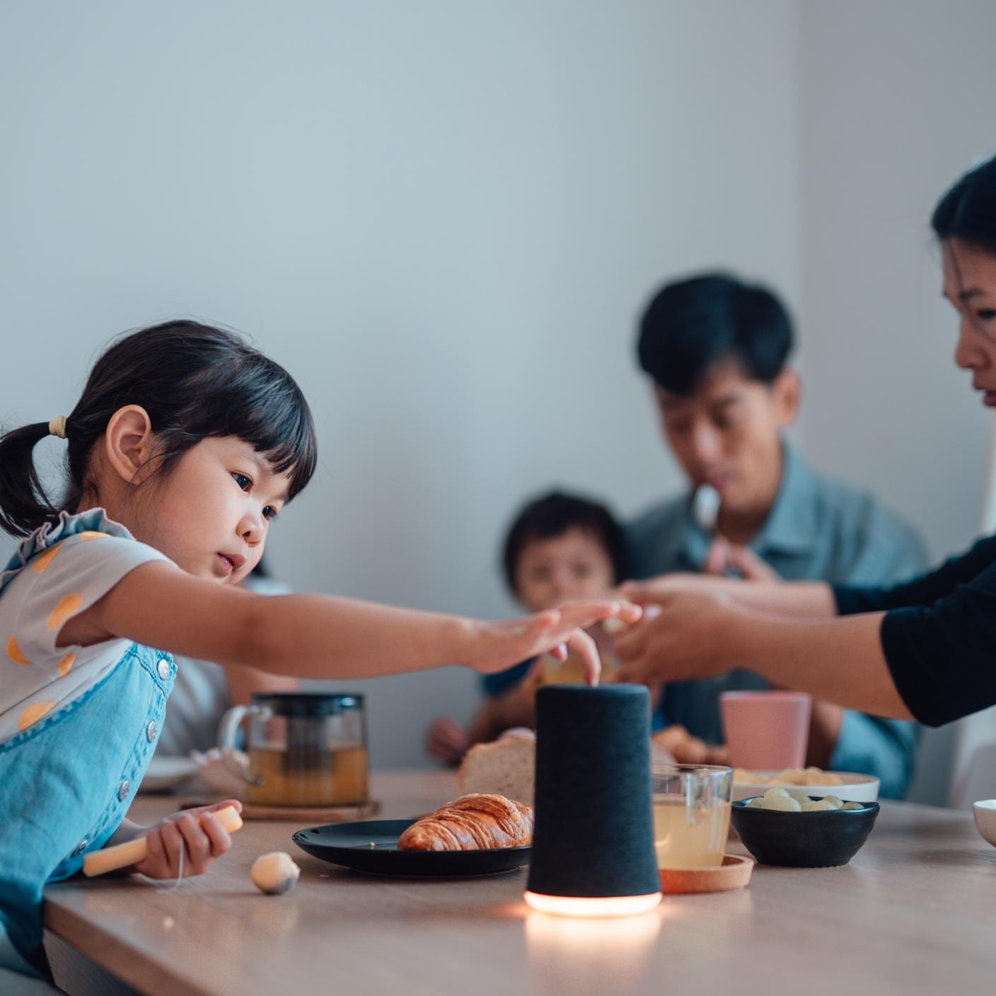 Young girl using smart speaker to play music while having breakfast at the table