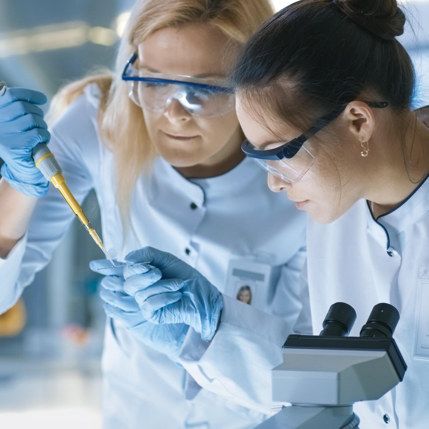 PAS 7062 - Medical Research Scientist Drops Sample on Slide and Her Colleague Examines it Under Microscope