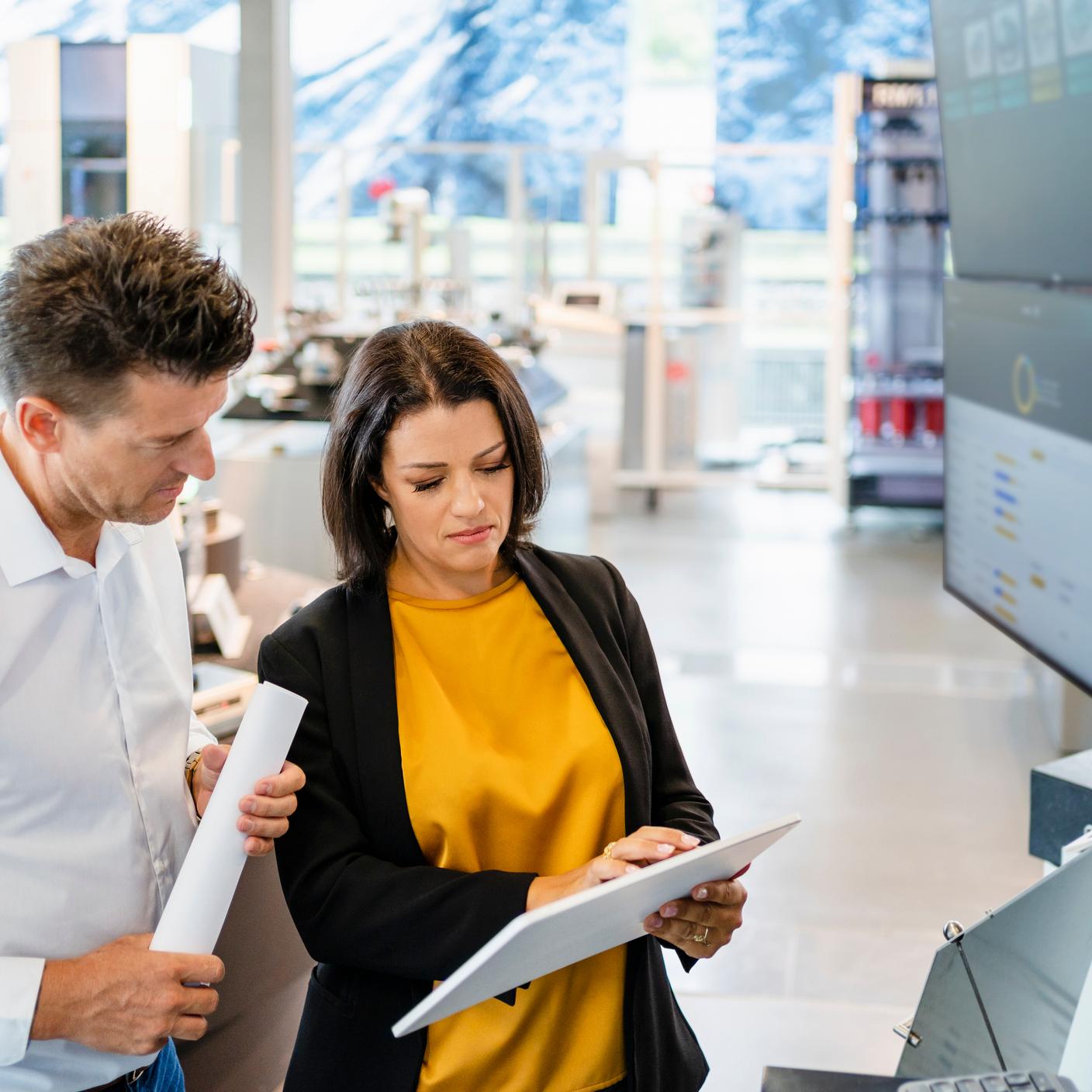 Helping UK manufacturing embrace digitalization - Businesswoman using tablet PC standing by colleague in industry