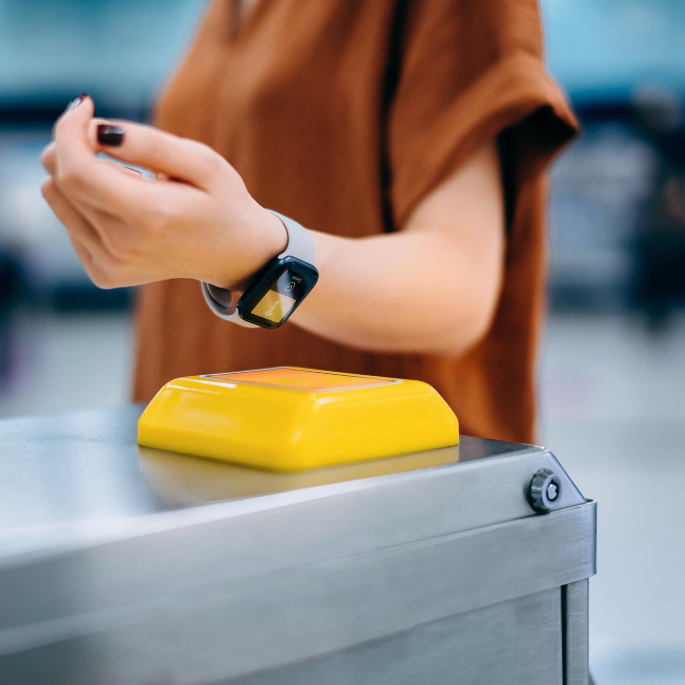 Woman checking in at subway station, making a contactless payment for subway ticket via smartwatch.