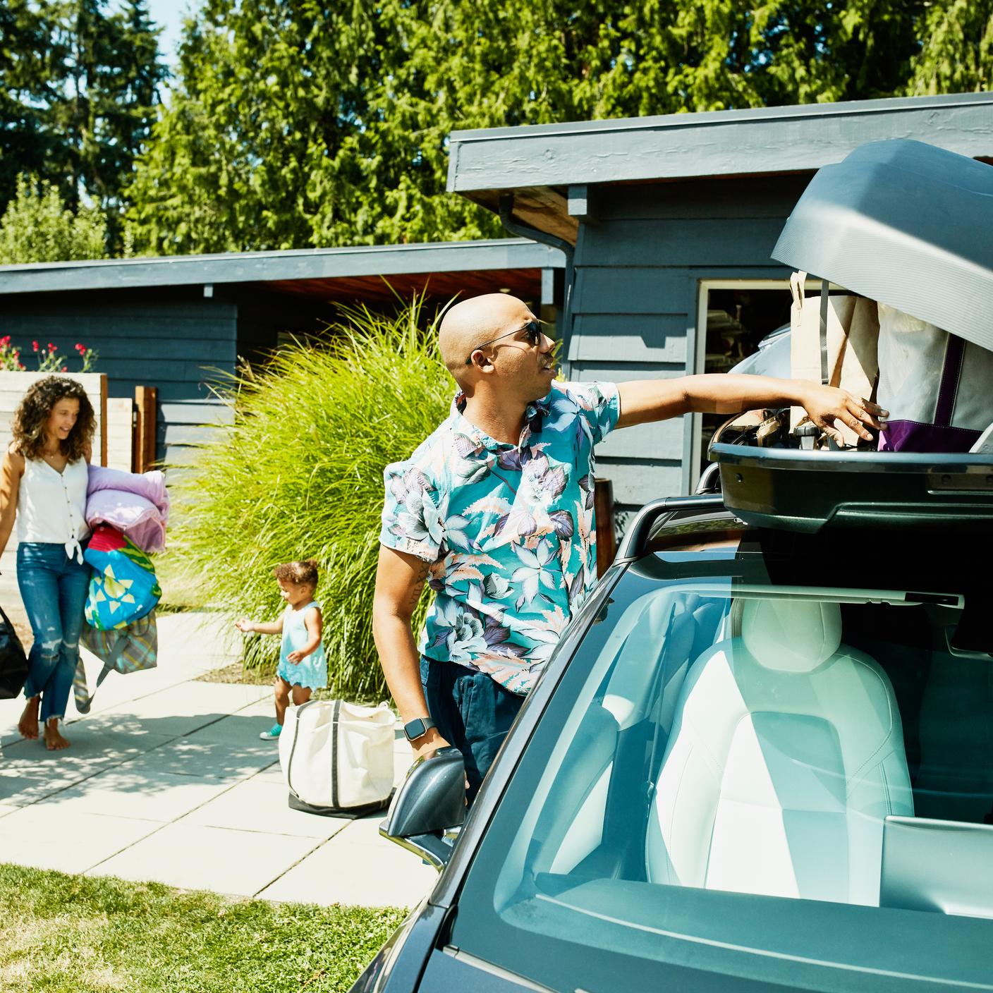 Family loading luggage into car top box before road trip