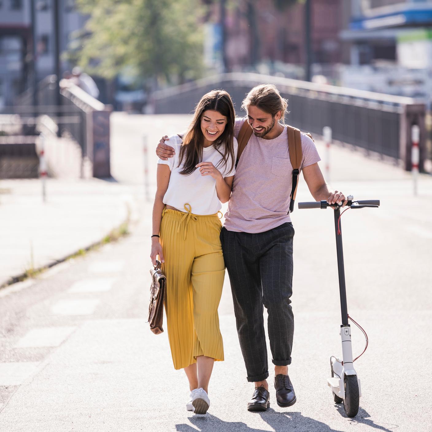 Sustainability in Transport and Mobility - Happy young couple with electric scooter walking on the street