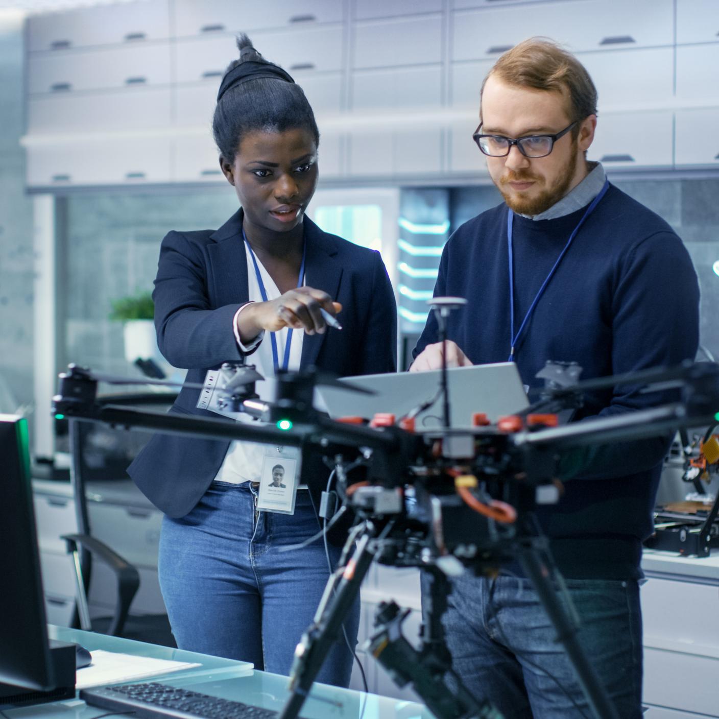 Caucasian Male and Black Female Engineers Working on a Drone Project with Help of Laptop