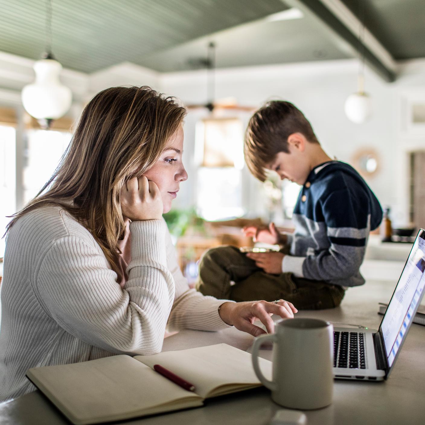 The Kitemark™ for inclusive service  - Woman working from home on laptop while son uses smartphone