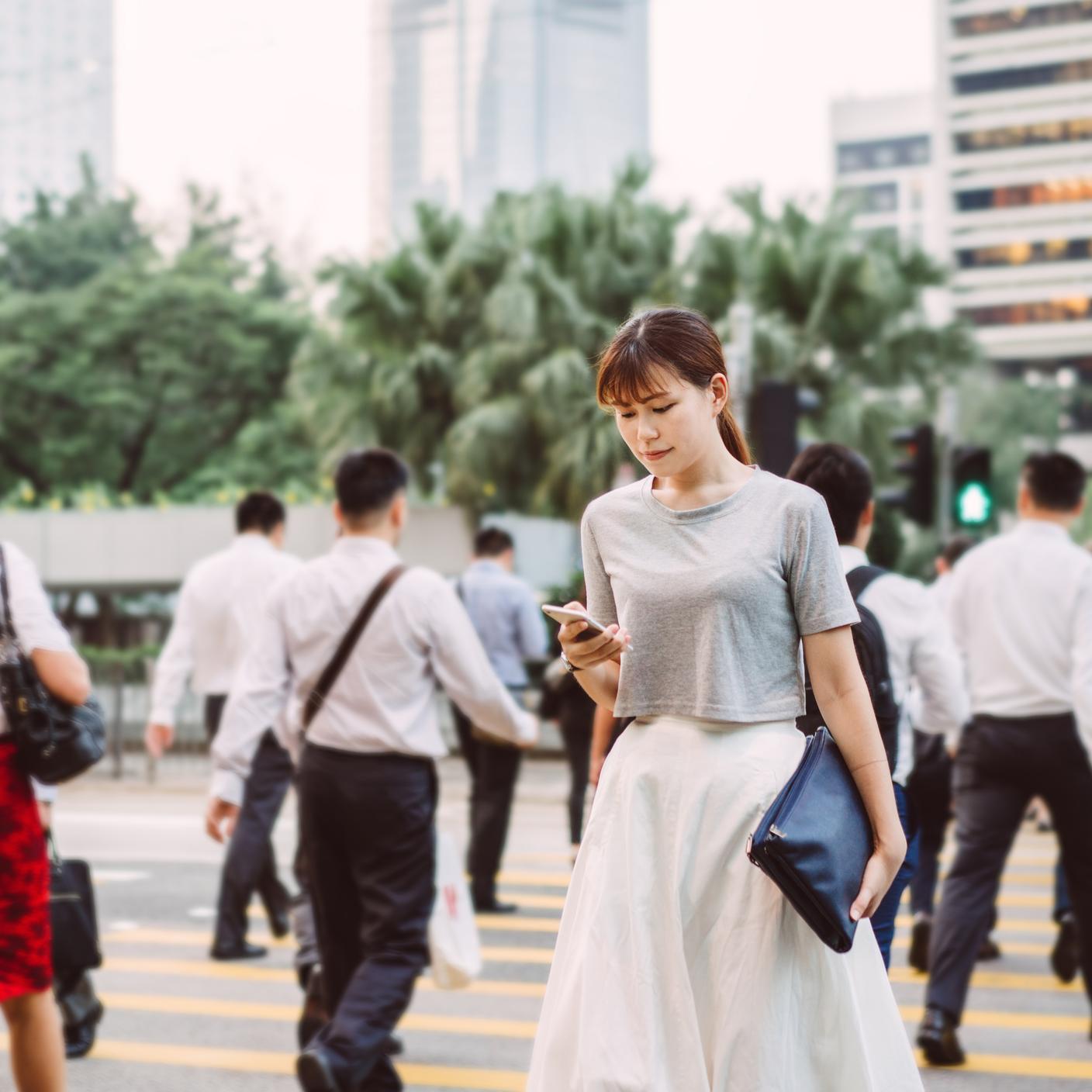 lady using smartphone while crossing the road in central business district