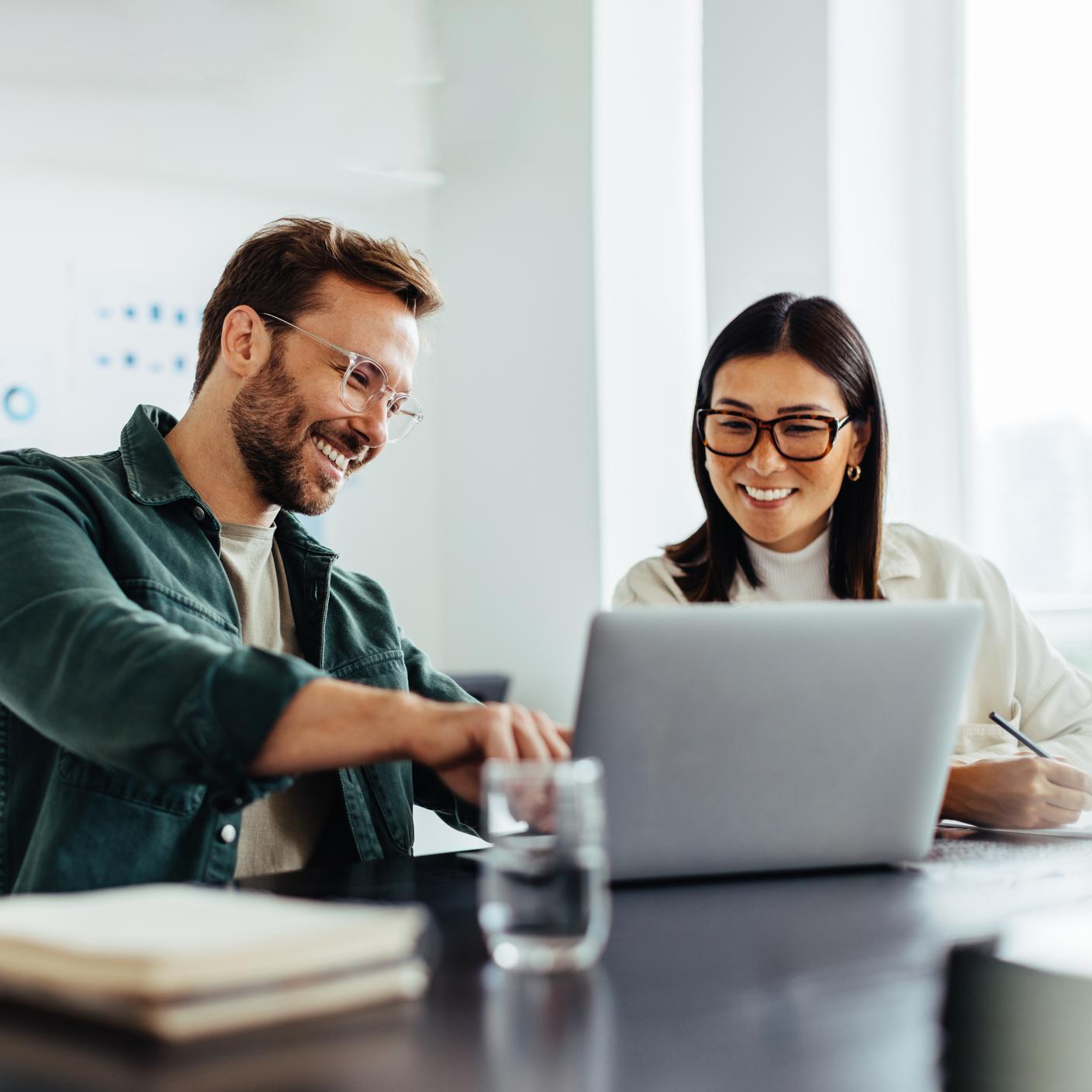 Two business people using a laptop together while sitting in a meeting