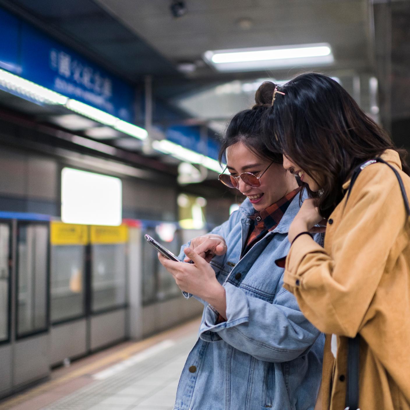 Women planning their travel on mobile phone, waiting on the subway station.