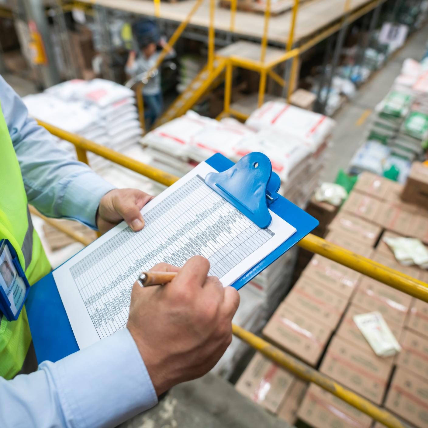 Close-up on an operator making an inventory at a distribution warehouse and writing on a clipboard