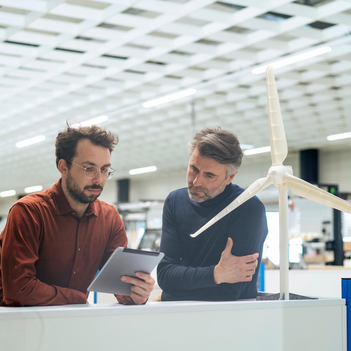 Worker using tablet next to wind turbine model 