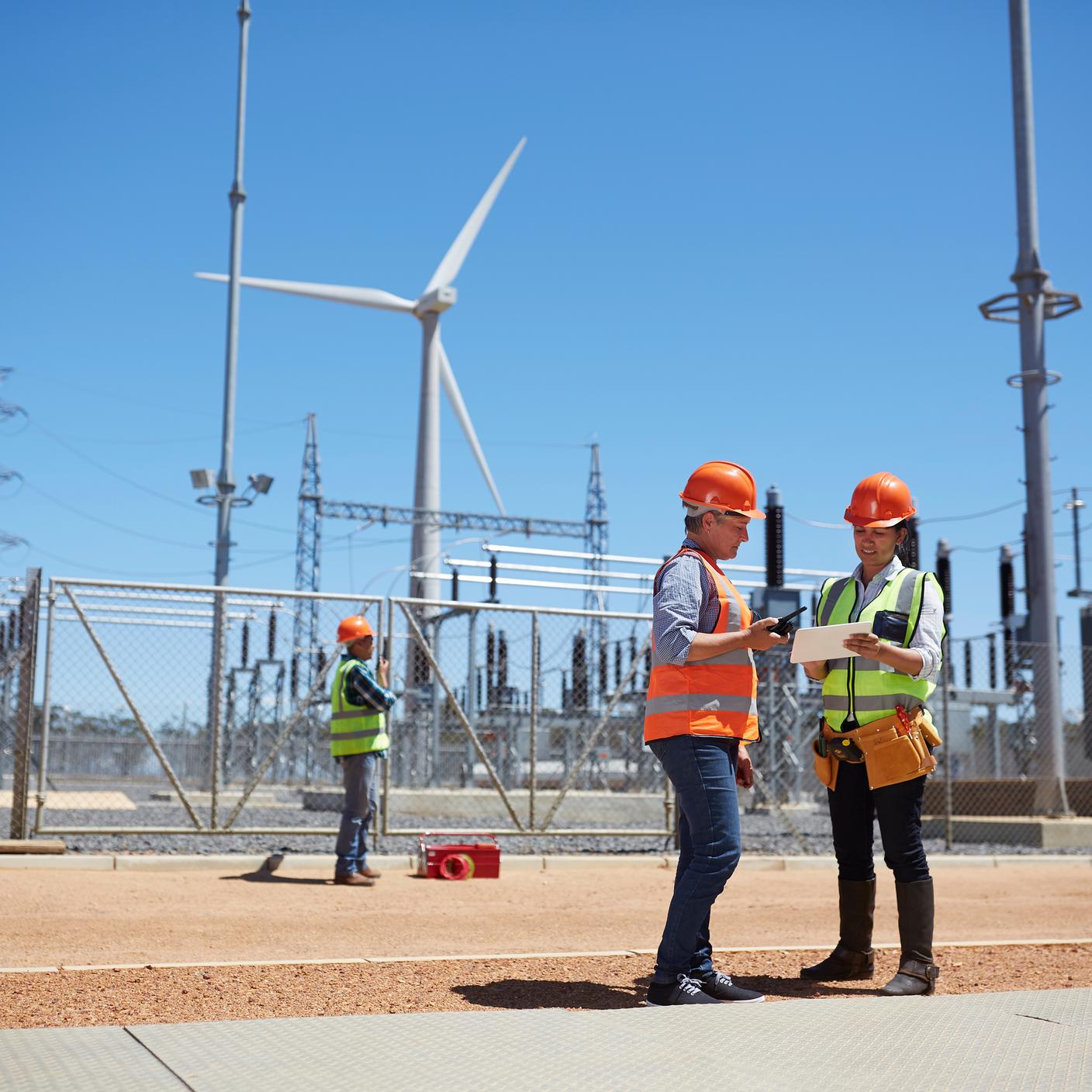 Engineers using digital tablet at sunny wind turbine power plant